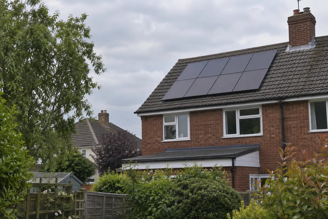 Solar panels on a brick house with a leafy tree and neighbouring roof in view.