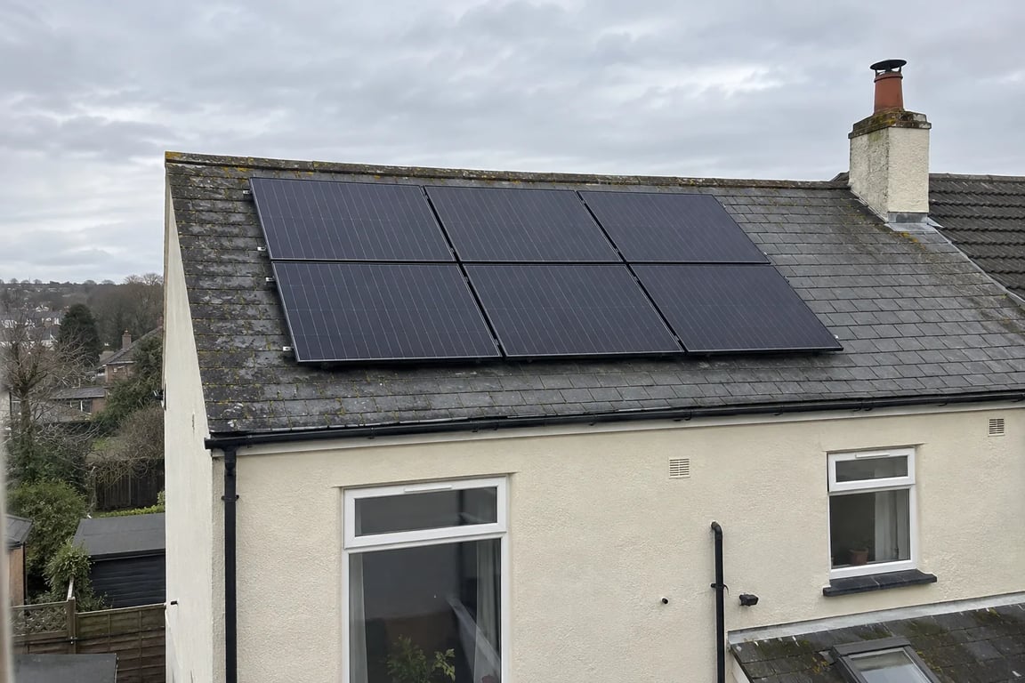 Six solar panels on a slate roof above a cream-rendered rear wall.